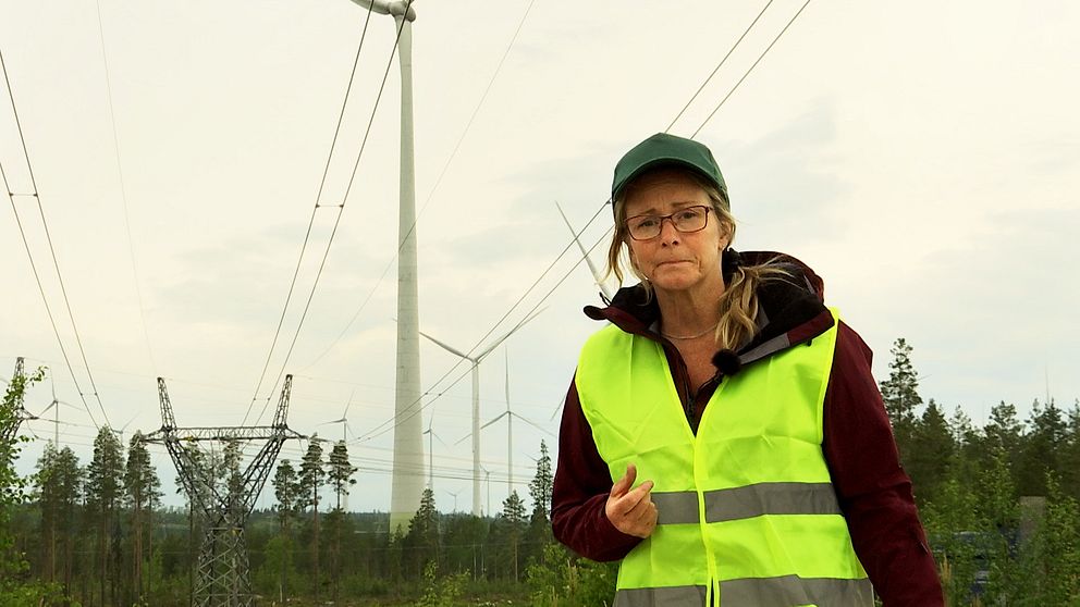 En kvinna i gul varselväst med vindkraftverk i bakgrunden.