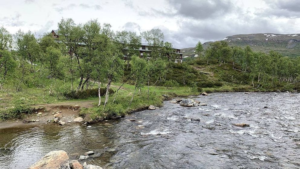 vy över vattendrag, gles björkskog, fjäll och den stora turiststationen som skymtar