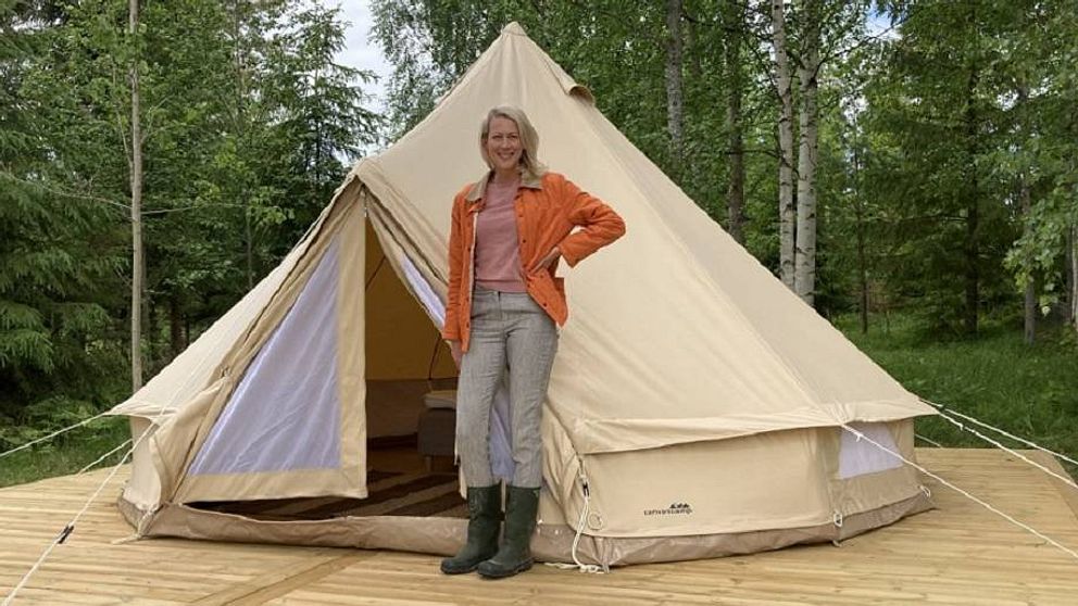 en kvinna står framför ett tält på ett trädäck med skog i bakgrunden