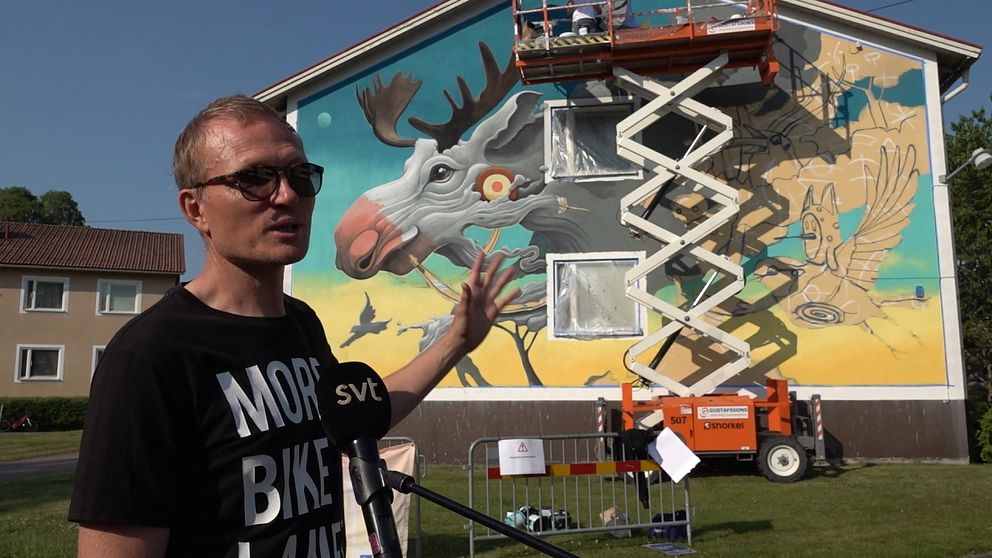 Albin Wiberg, projektledare, framför spanska konstnären Dulks målning på ett hyreshus i lilla samhället Hjorted.