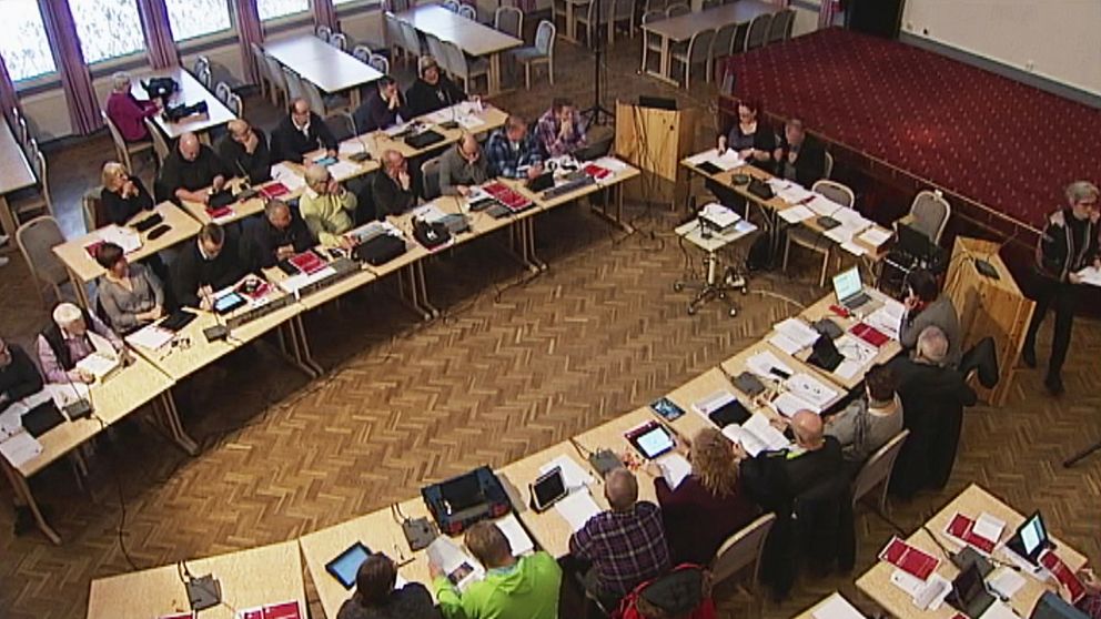 Massvis av människor som sitter runt två avlånga bord med datorer och papper framför sig. Det är ett kommunfullmäktige-möte i Övertorneå.