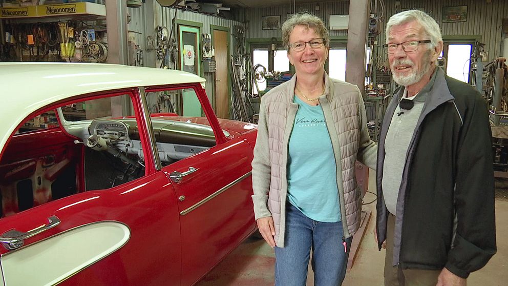 ett äldre par vid en veteranbil i ett verkstadsgarage