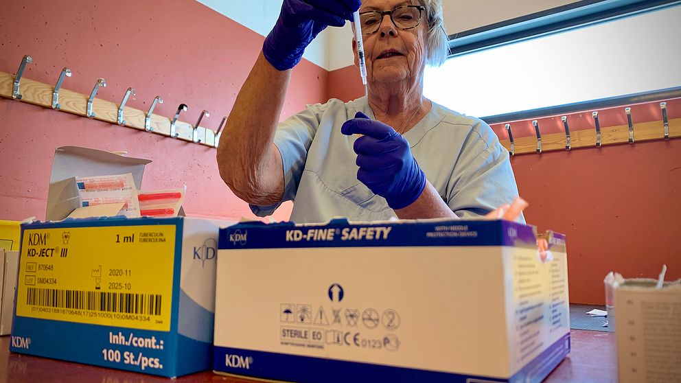 en äldre medelålders kvinna i vårdens kläder och gummihandskar med en vaccinspruta, kartonger i förgrunden