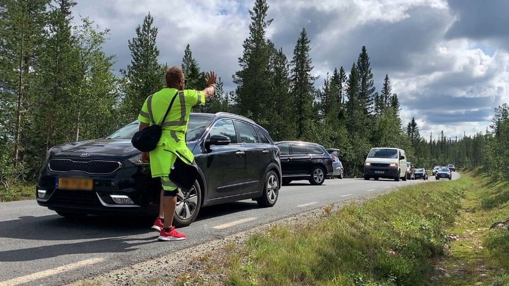 En parkeringsvakt håller upp handen och ber bilar vänta.