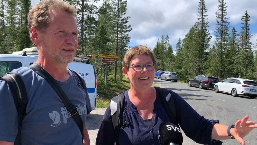 Två personer står vid Fulufjällets nationalpark. I bakgrunden ser man mängder av bilar parkerade.