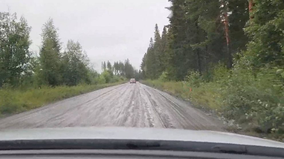 Bil färdas på dålig grusväg i regn.
