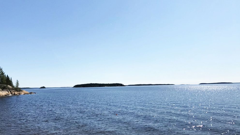 På bildens syns ett blått hav och blå himmel. I bakgrunden kan man skymta små öar.