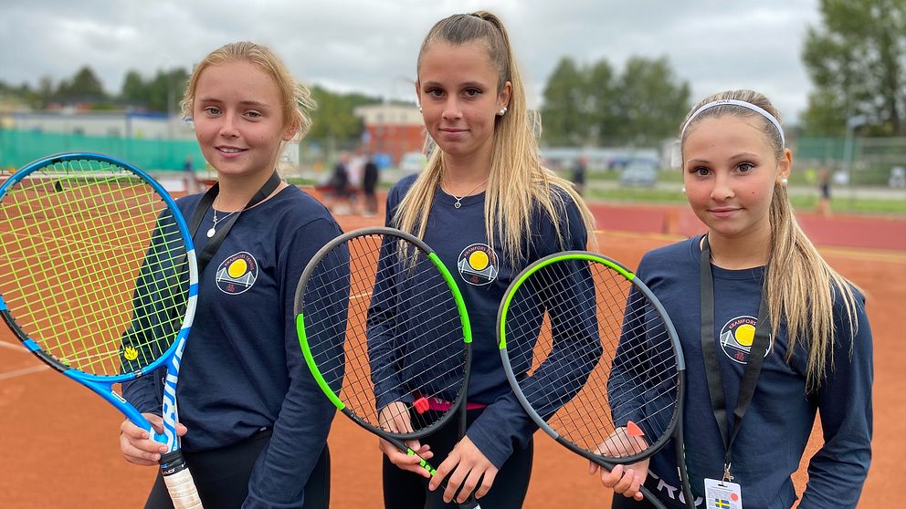 Anna Gymnander, Gabriella Danielsson och Isabelle Danielsson står i blå tröjor med Kramfors tennisklubbs logga på. De håller i varsinn racket och tittar in i kameran.