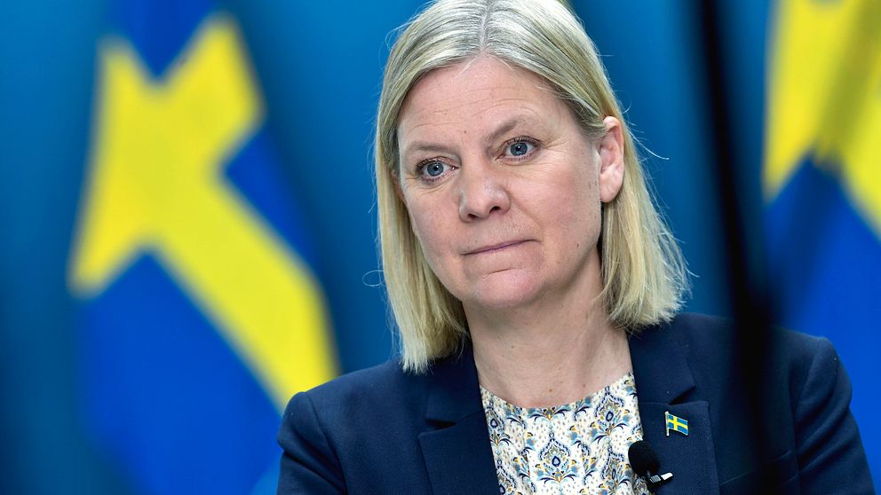 Finansminister Magdalena Andersson tittar åt höger. I bakgrunden syns suddiga svenska flaggor.