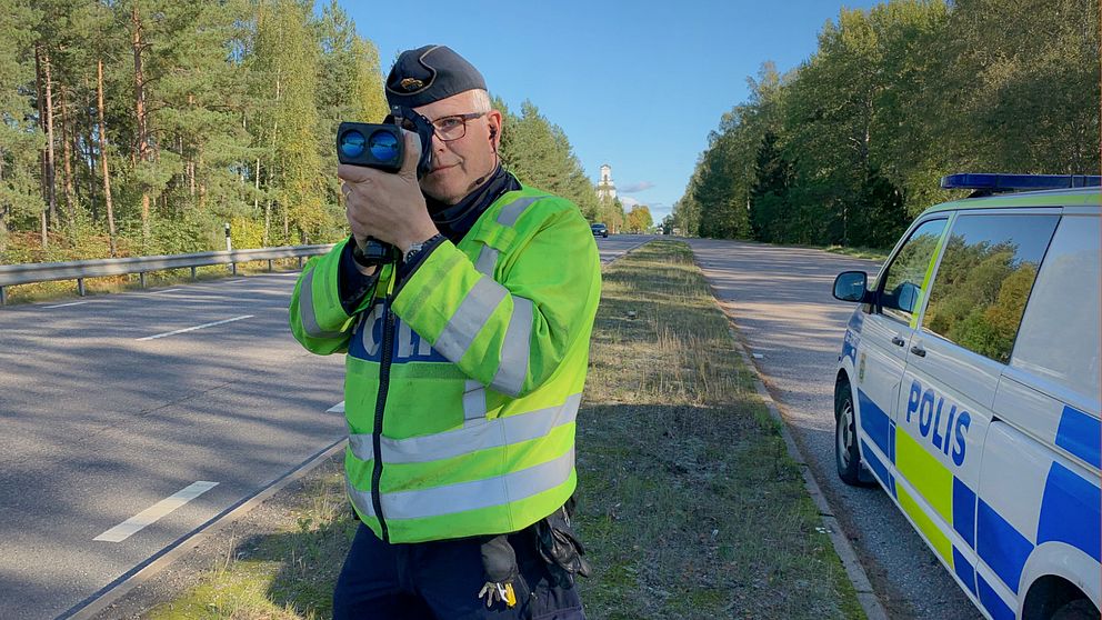 Trafikpolisen Lars Österberg som står bredvid en polisbil och skjuter med laserkikare på förbipasserande bilar.