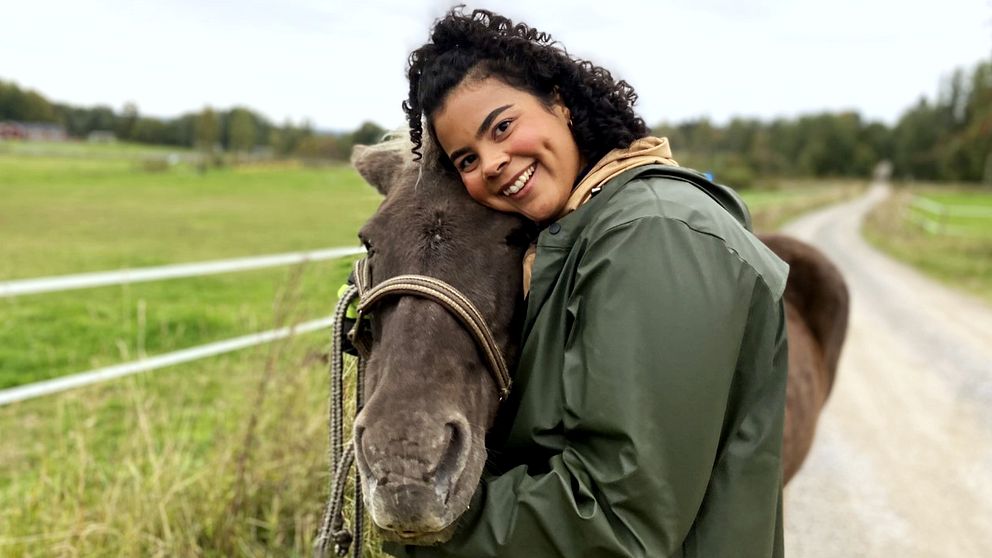 En leende Isabel Neib står till höger i bild och kramar en häst som står bredvid henne. De tittar in i kameran.