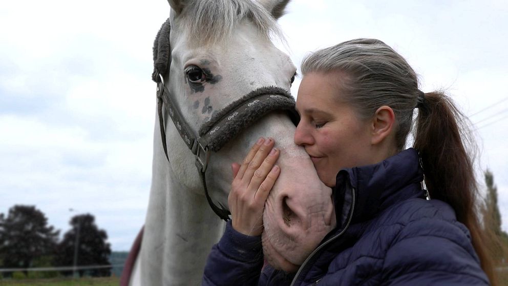 en medelålders kvinna gosar med en vit häst i hagen