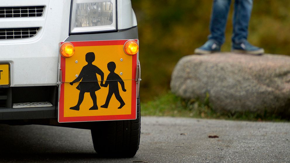 närbild på skylt på en skolskjuts-bil, i bakgrunden syns fötterna på en pojke som står på en sten
