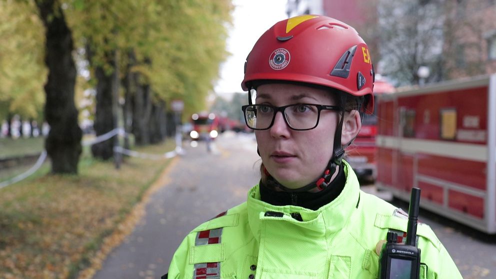 en kvinna i räddningstjänstens hjälm och varseljacka, walkie-talkie på axeln
