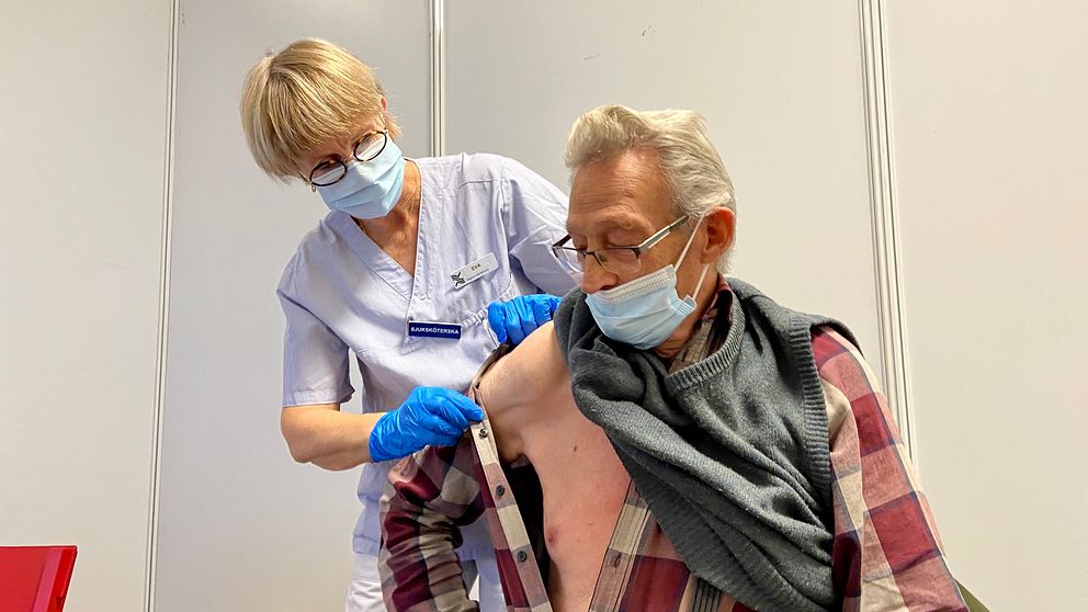 Sjuksköterska drar undan skjortan på en herre för att ge denne en vaccinspruta.