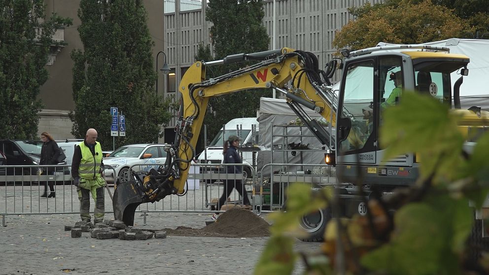 Gul grävmaskin gräver ett hål i marken på Stora torget i Västerås.
