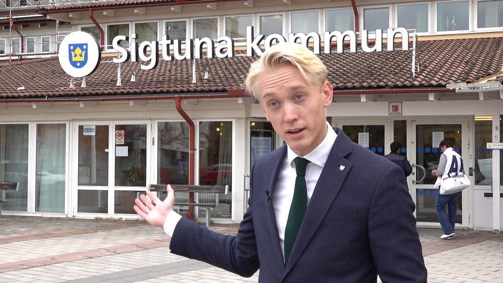 Mattias Askerson står framför kommunhuse. Med ena handen visar han det bakom.