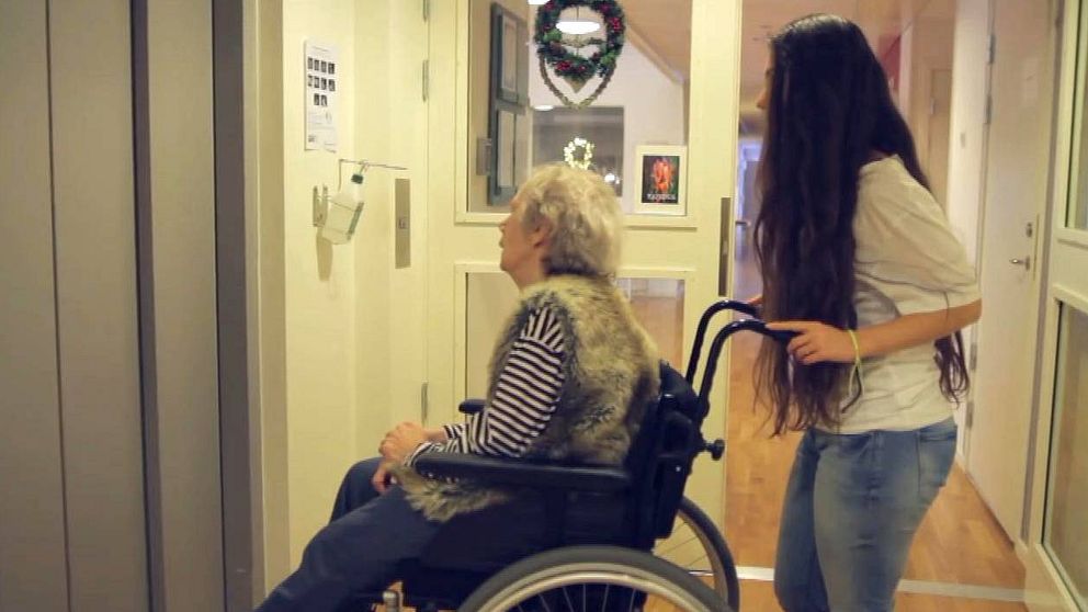 En ung kvinna står bakom en äldre kvinna som sitter i rullstol.