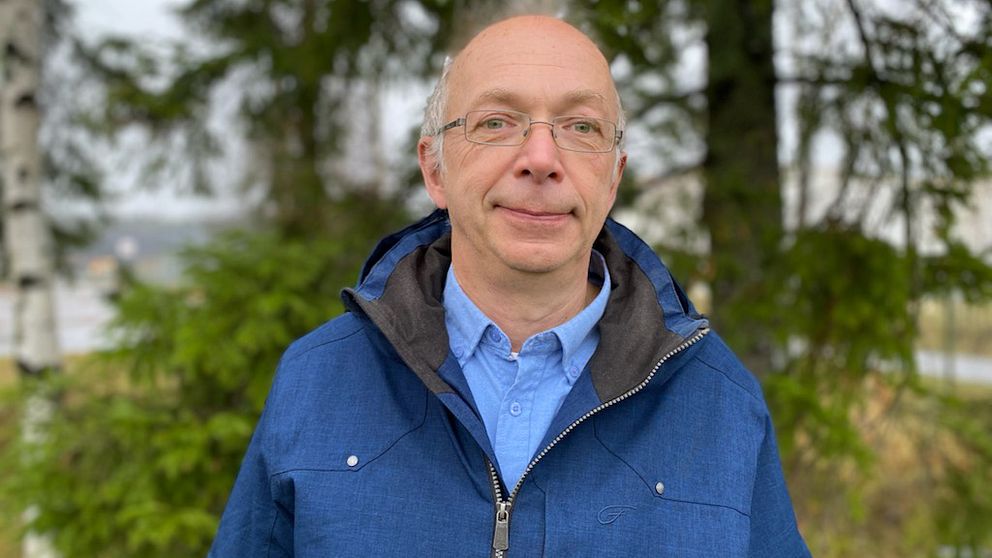 En man i blå jacka står framför några träd