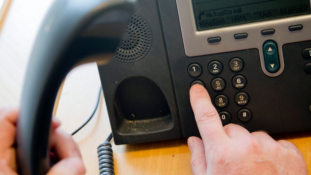 En person lyfter en telefonlur och har lagt ett finger på nummerpanelen för att slå ett nummer.