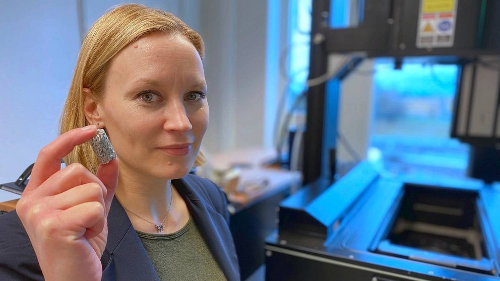 Professor Cecilia Persson står vid en 3D-laserskrivare och håller upp en benreplika av magnesium.