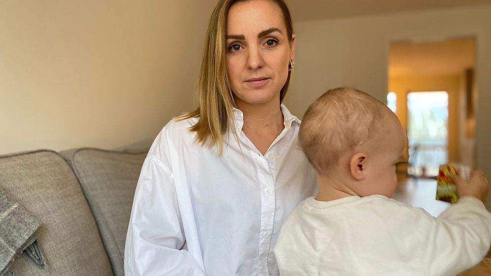 Mamma Micaela Gyllerström har sin dotter i knät. Hon har på sig en vit skjorta och sitter på en ljus soffa, bakgrunden är suddig. Dotter tittar bort från kameran.