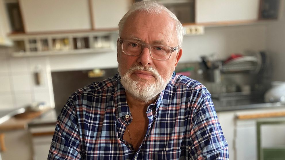 En bild på Staffan Lagerström som sitter i sitt kök. Han är en man i 75-årsåldern med vitt hår och vitt skägg.