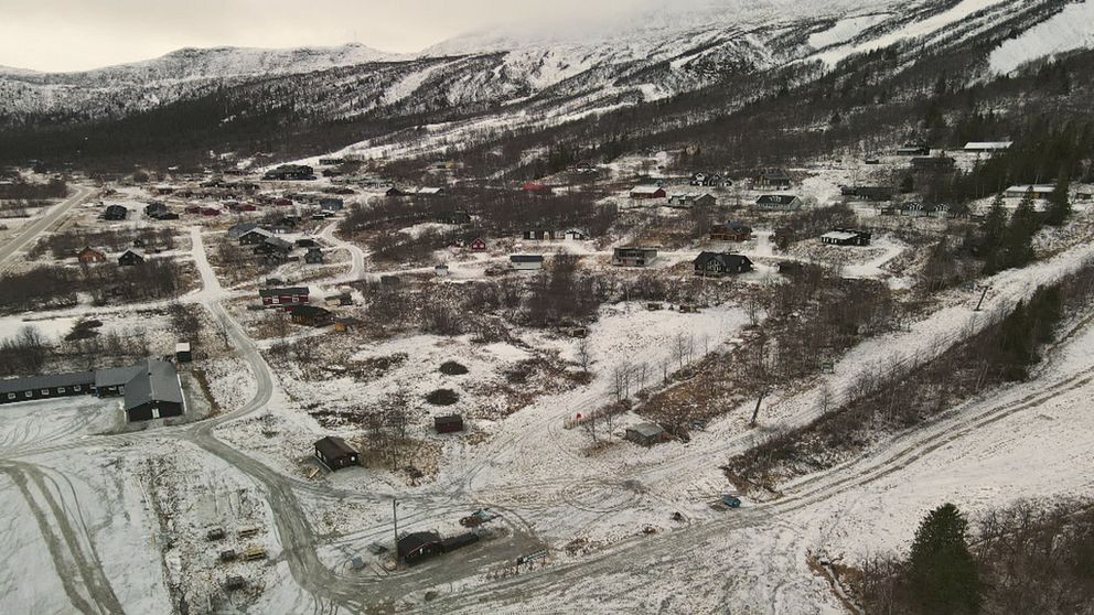 En drönarbild på ett snöigt, glest bygt bostadsområde omgivet av fjäll.
