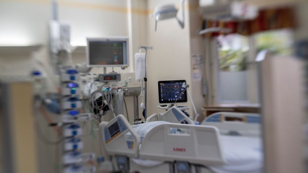 En sjukhussäng med tillhörande skärmar och slangar syns suddigt.
