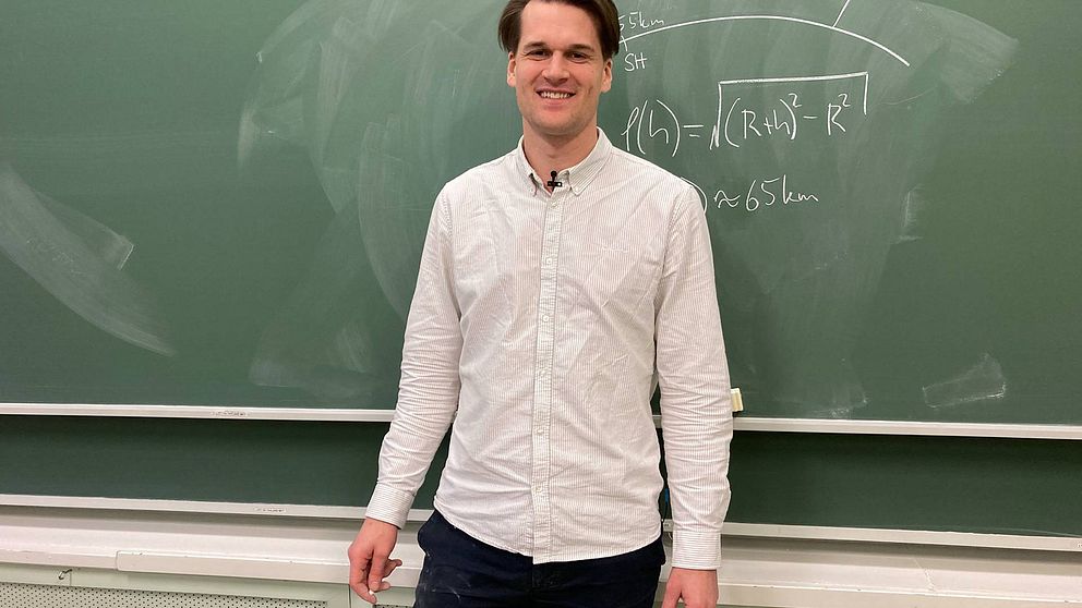 Man framför griffeltavla med matematisk formel skriven på.
