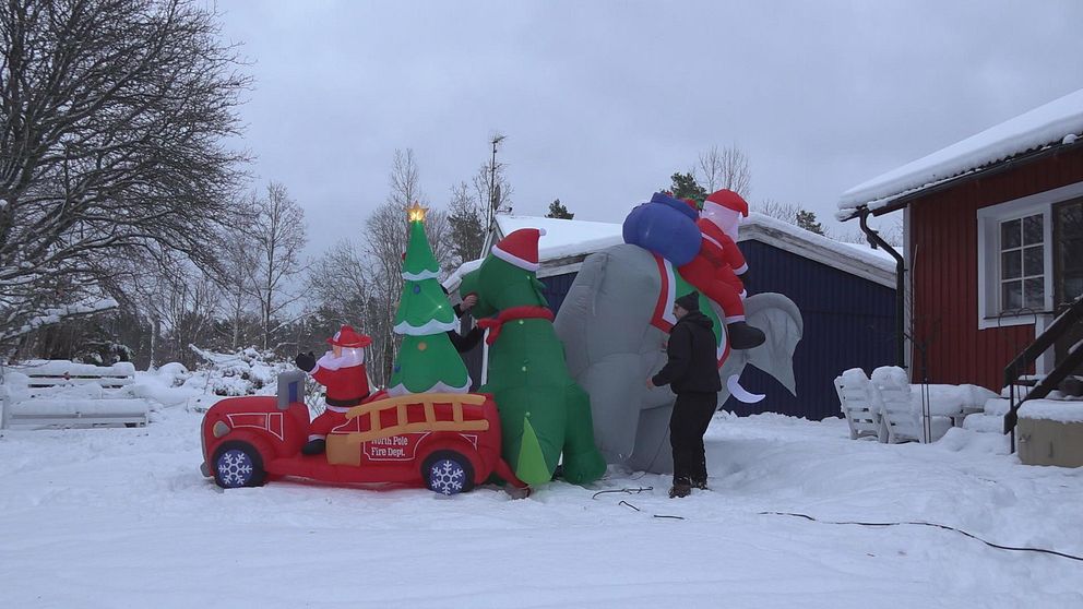 På bilden står tre uppblåsbara juldekorationer ute i snön i en trädgård. En elefant med en tomte på ryggen, en dinosaurie med tomteluva och en tomte som kör brandbil. Bredvid elefanten står julfantasten Mathias Ripheden från Nybro.
