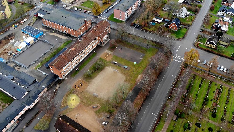 Luftfoto över en skolgård med omgivande byggnader och vägar.