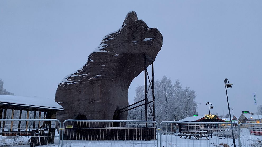 en stor, hög, björn-liknande skulptur i trä, stagad med stöttor och inhägnad. Det snöar