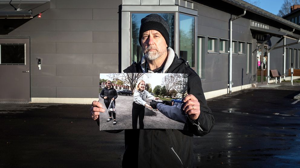 Man i mössa och skägg håller upp bild på flicka som tar emot något.