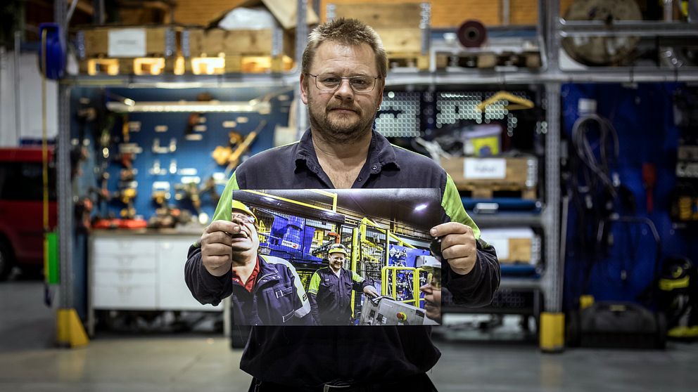 en man i verkstadsmiljö håller upp en bild på skrattande människor i verkstadsmiljö