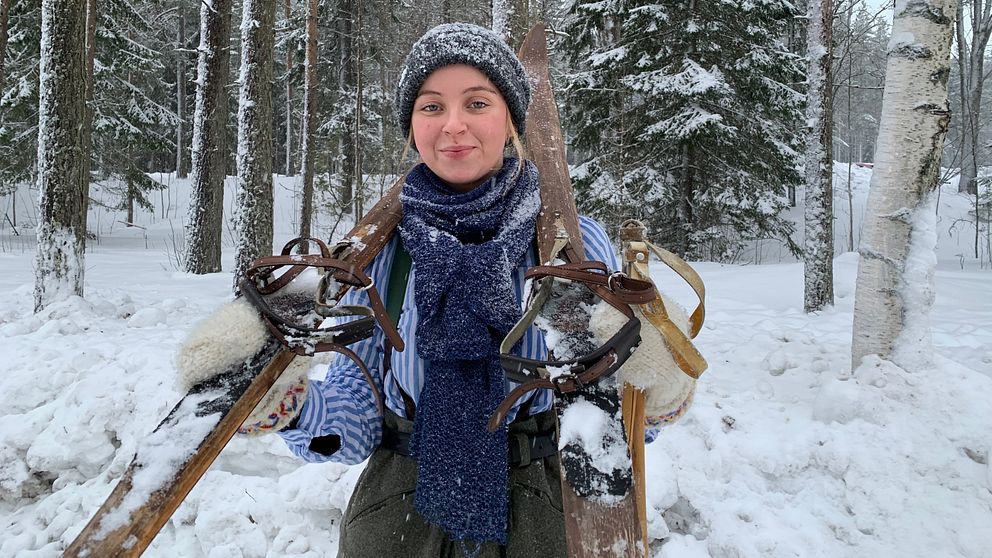 En kvinna med snöiga kläder håller i gammal skidutrustnung.
