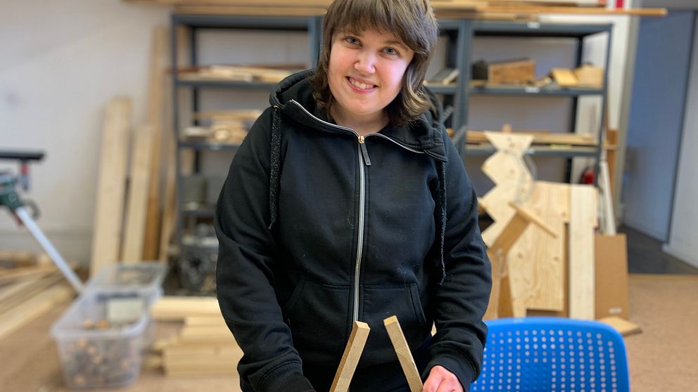 Helena står i en snickarverkstad och ler stort mot kameran.