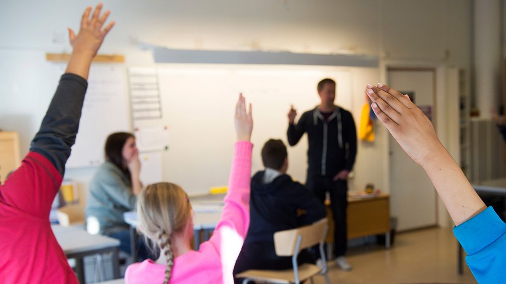Elever räcker upp handen i ett klassrum.