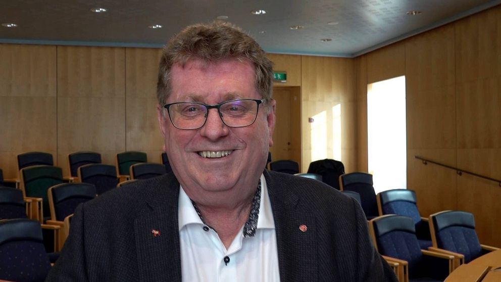 en leende medelålders man i kavaj och glasögon i en hörsal.