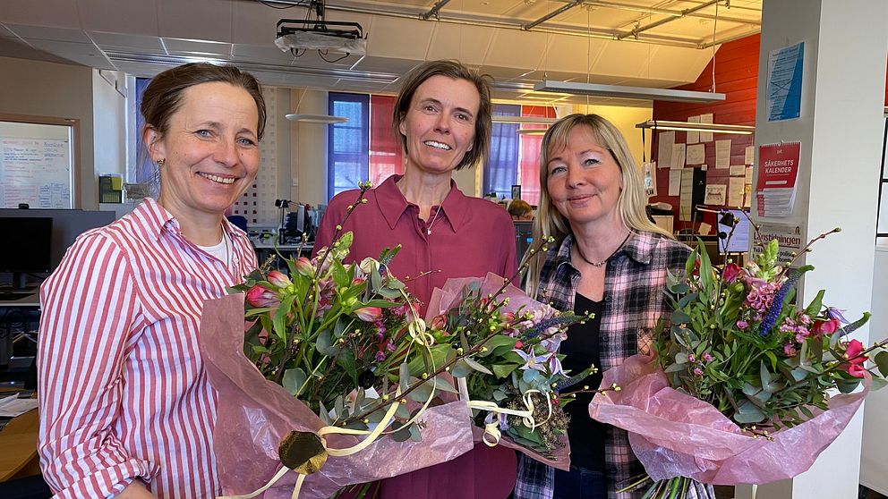 Tre kvinnor står bredvid varandra med blomkvastar. De är glada.