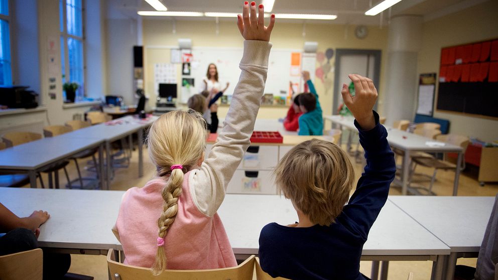 Barn som räcker upp handen i ett klassrum.