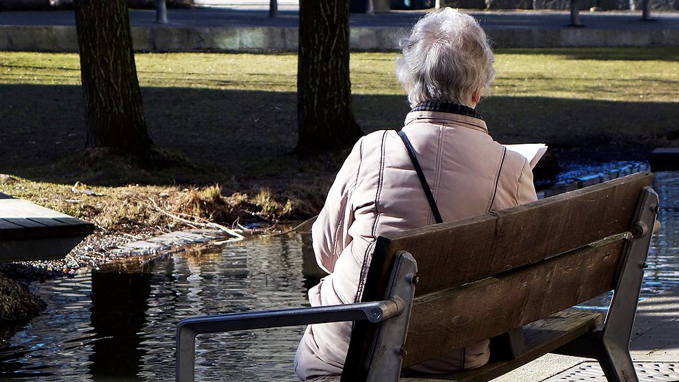 Äldre kvinna sitter på en bänk, med huvudet vänt bort från kameran.