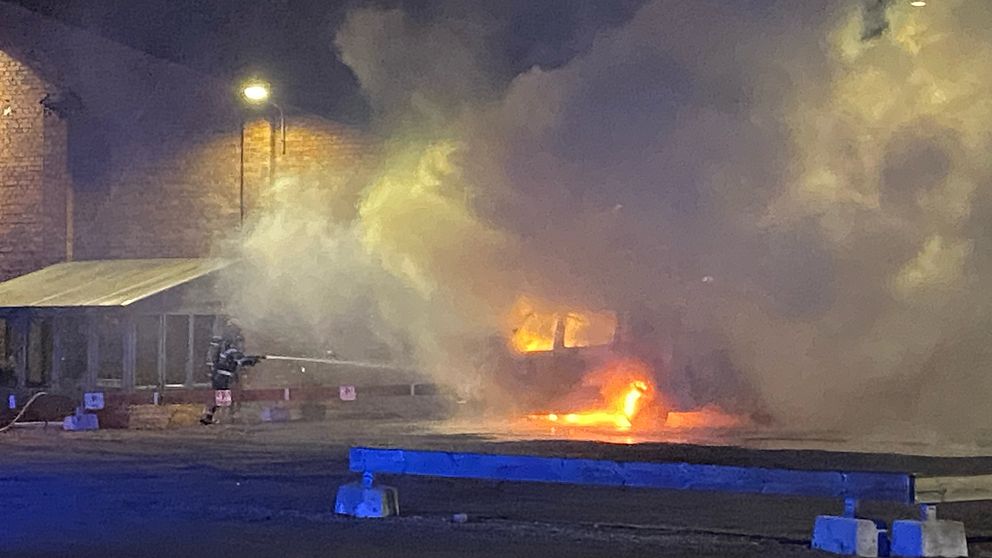 Bild på en brandman som sprutar vatten på en brinnande bil. Det är mycket rök.