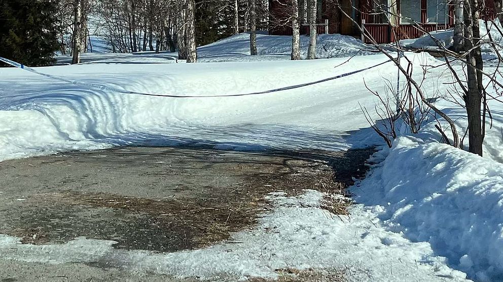 polisband över en uppfart med lite träd och snötäcke, trästuga skymtar