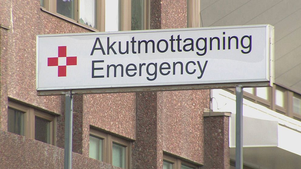 Vit rektangulär skylt med texten ”Akutmottagning Emergency” i svart text.