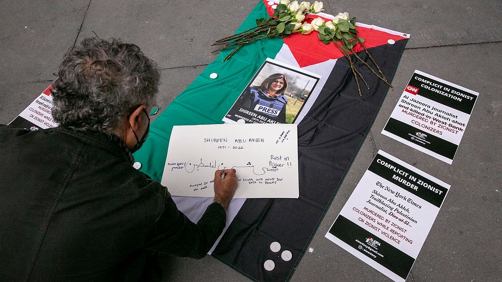 En man skriver ett meddelande till den palestinsk-amerikanska journalisten Shireen Abu Akleh under ett minnesmärke och en demonstration till hennes ära utanför The New York Times kontorsbyggnad i New York, USA på fredagen.