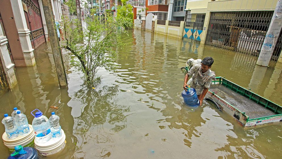 En man levererar dricksvatten till hus längs med en översvämmad gata i Sylhet, Bangladesh.