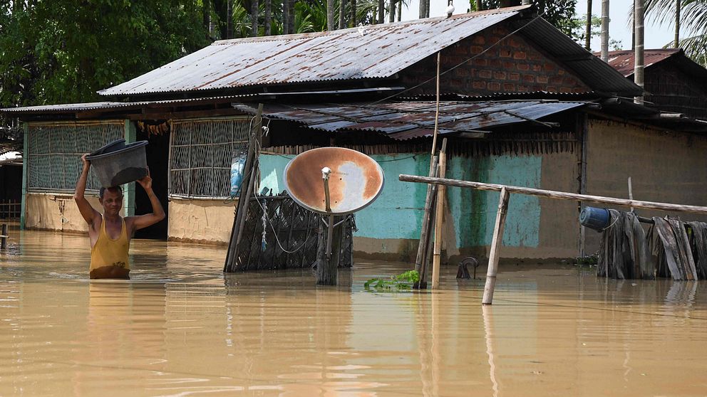 Bilden visar en man som bär sina tillhörigheter genom ett översvämmat område i Indien.