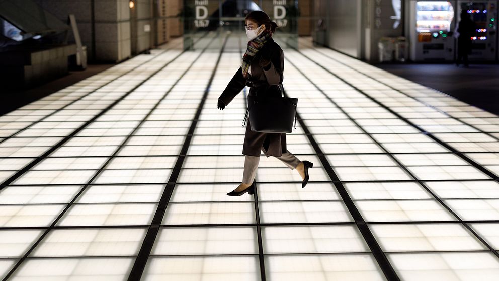 En kvinna bär ansiktsmask på väg in i Tokyos tågstation.