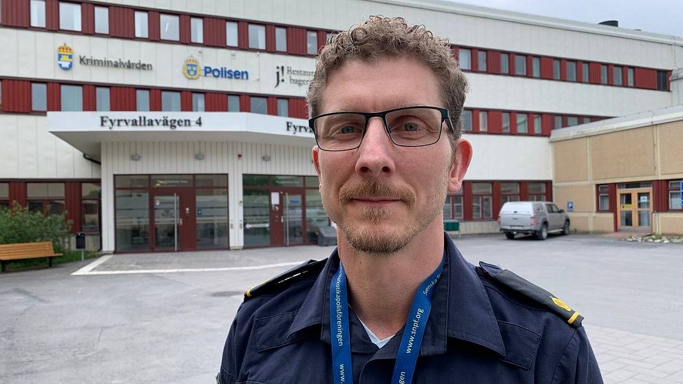 Polisman med lockigt kortklippt brunt hår och glasögon. Han står framför polishuset i Östersund.